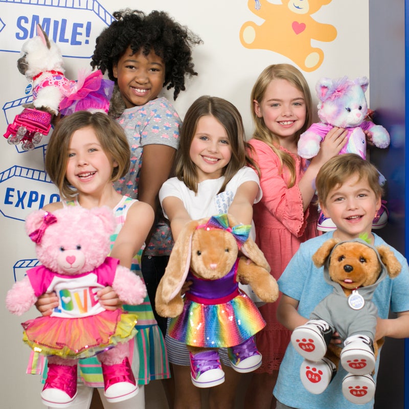 Children holding stuffed animals in front of a colorful wall with text